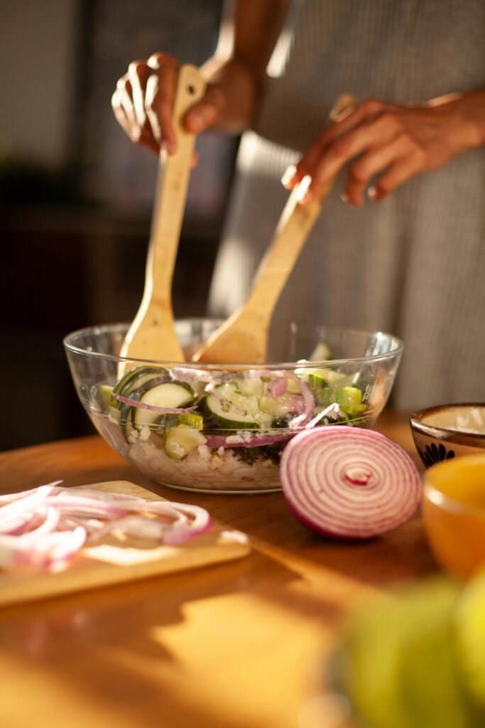 A fresh zucchini and onion salad being mixed in a glass bowl with wooden spoons indoors.